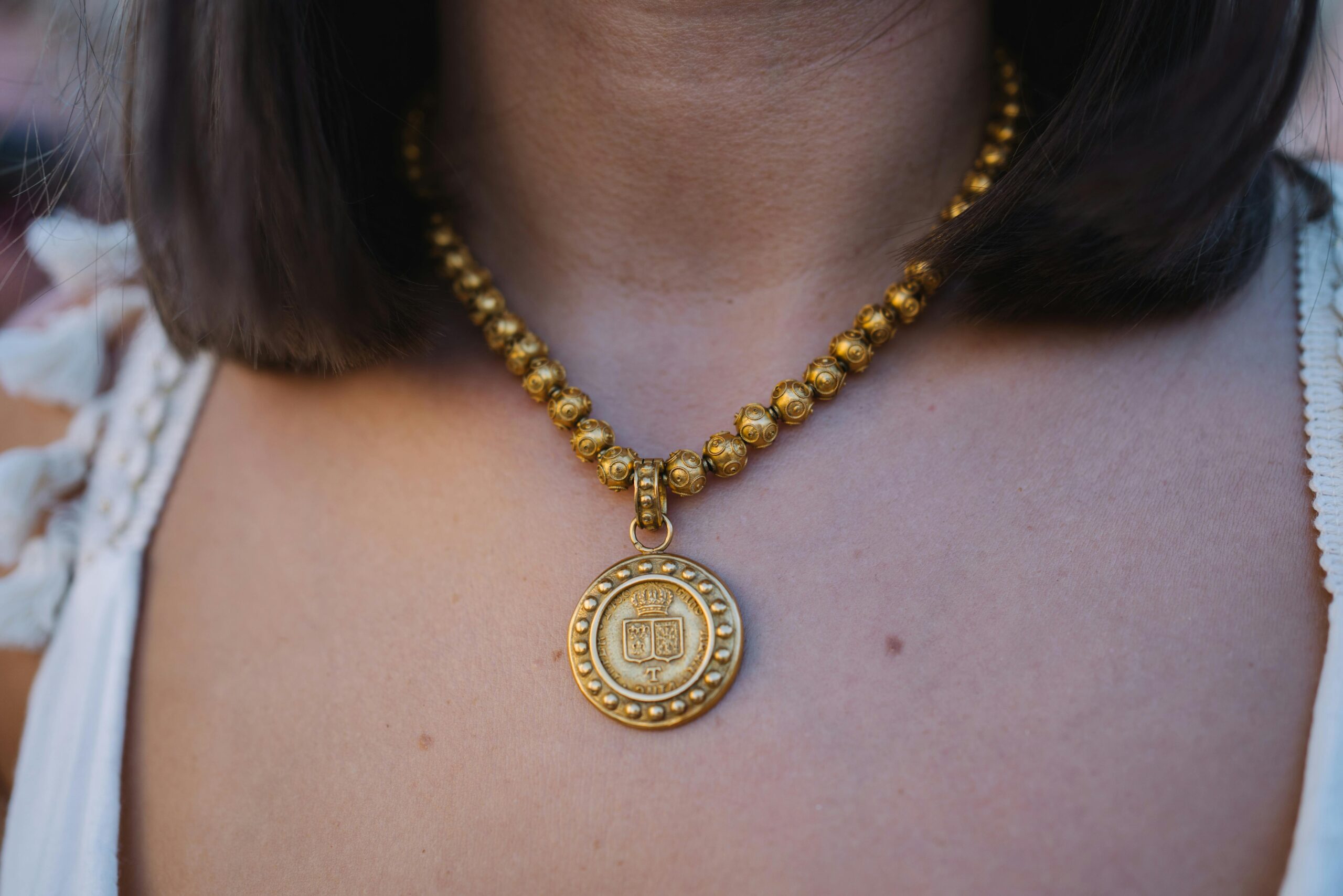 Close-up of a woman wearing a luxurious gold beaded necklace with an intricate pendant.